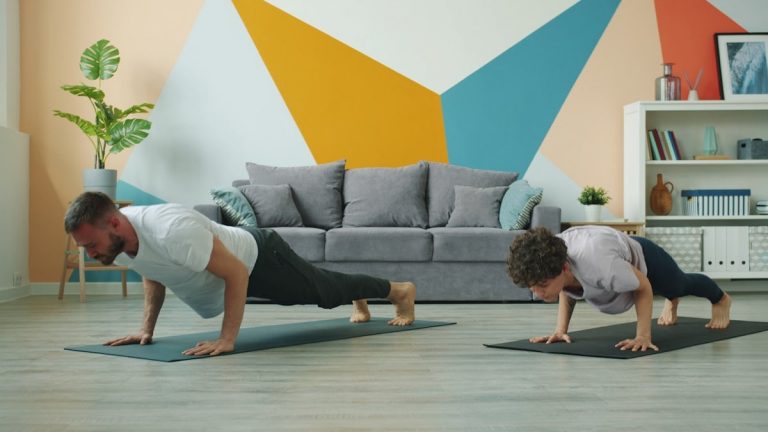 Male and female yoga students are practising downward dog position at home focused on practice on mats, people are moving simultaneously doing asanas.