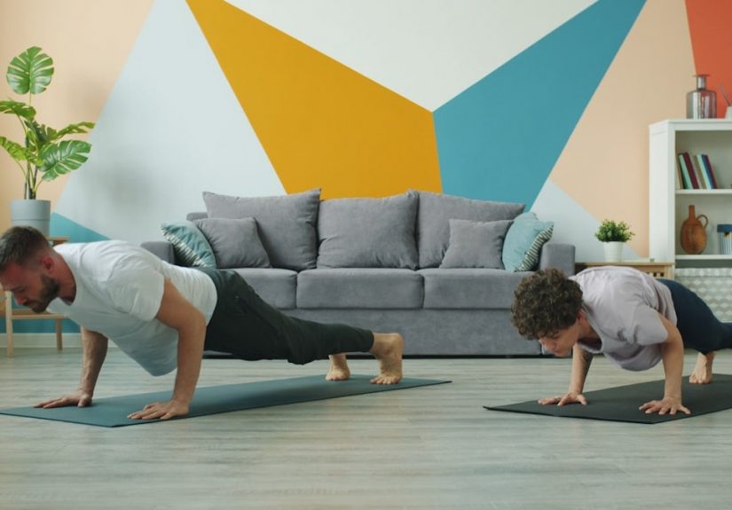 Male and female yoga students are practising downward dog position at home focused on practice on mats, people are moving simultaneously doing asanas.